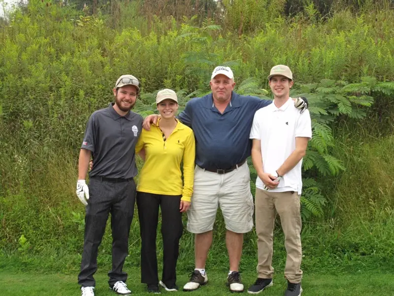 A group of four people, two men and two women, standing together in a grassy outdoor setting.